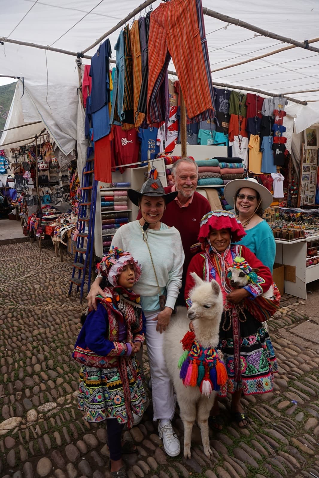 Donna Atmore, Kim Yost, and Terie Spencer at a Peruvian market with locals in traditional Quechua dress and a baby llama